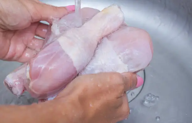 Photo of Woman washing raw frozen hen in kitchen sink. Cooking chicken at home. Close-up, selective focus.