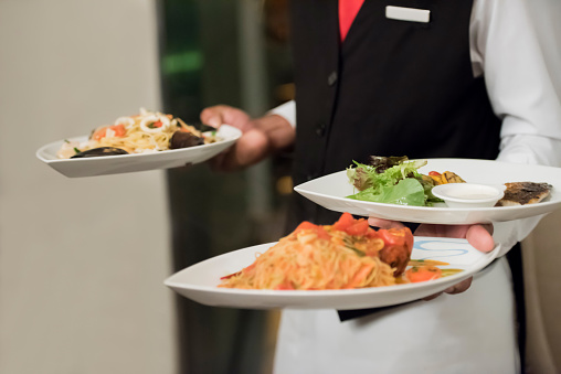 Close up photo of waiter dressed in suit and tie serving multiple plates in high end restaurant, selective focus