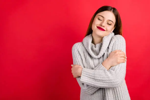 Photo of Pretty overjoyed lady with closed eyes touching soft knitted jumper isolated on red background