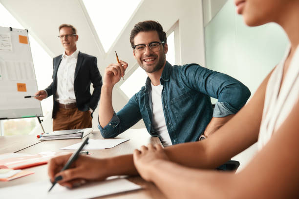 istock I love my team. Young and handsome man looking at camera with smile while his boss standing near whiteboard and explaining something on the background 1173522459