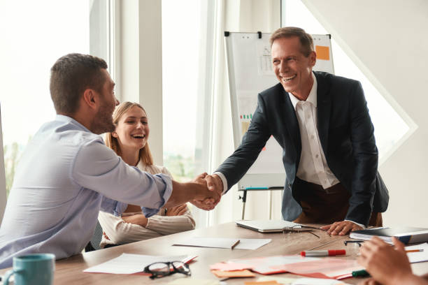 istock Welcome! Two cheerful colleagues shaking hands and smiling while sitting in the modern office 1173522500