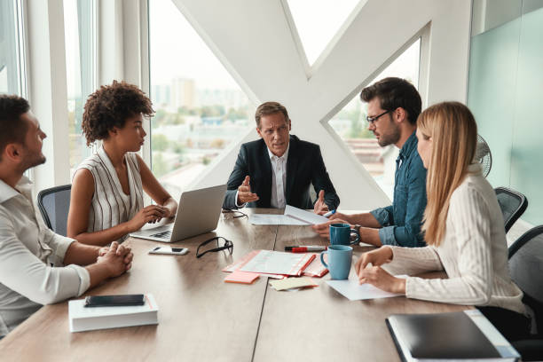 istock Morning meeting. Serious mature man discussing new project with multicultural team while sitting at the office table 1173524007