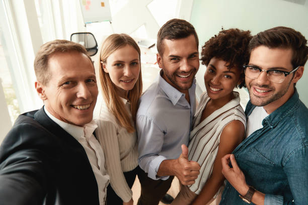 istock Group of cheerful colleagues taking selfie and gesturing while standing in the modern office 1173524349