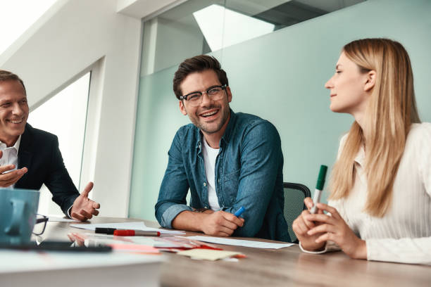 istock We have great results! Young handsome man in eyeglasses discussing something with colleagues and smiling while sitting in the modern office 1173524361