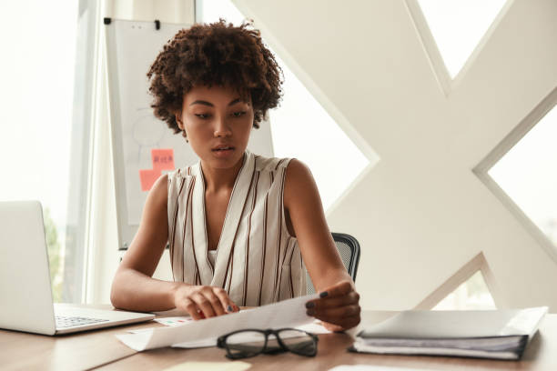 istock Young expert. Beautiful afro american woman analyzing documents while sitting in modern office 1173524530