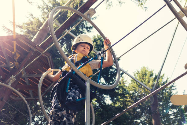 poniżej widok chłopca przekraczania przeszkód podczas zip podszewka w lesie. - zip lining zdjęcia i obrazy z banku zdjęć