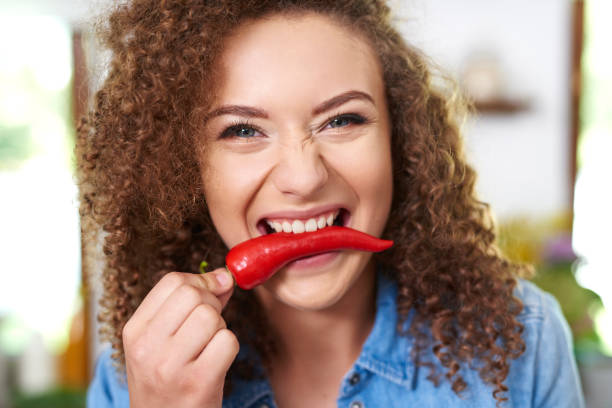 mujer sosteniendo pimienta roja en su boca - human mouth human teeth indoors young women fotografías e imágenes de stock