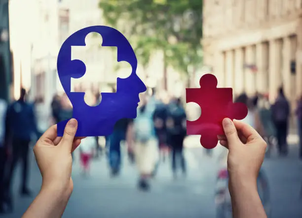 Photo of Two hands holding a paper with human head and a puzzle piece. Finding a cure to heal the disease. Mental health concept, memory loss and dementia disease. Alzheimer's losing brain and memory function.