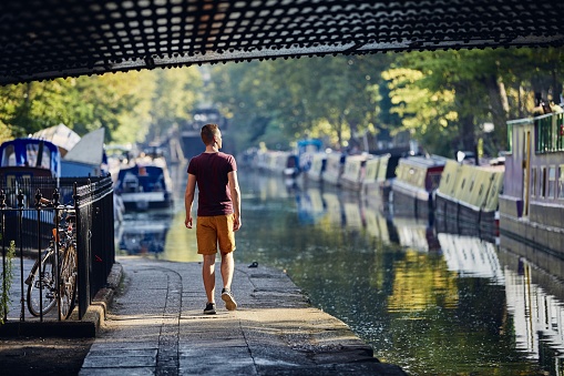 Young man walking on waterfront of Regents canal with boats. Little Venice in London, United Kingdom.