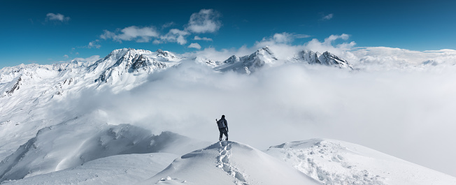 Man standing on the top of a snowcapped mountain peak. Panoramic view.