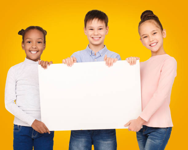 istock Happy kids showing blank placard board, yellow background 1173545144