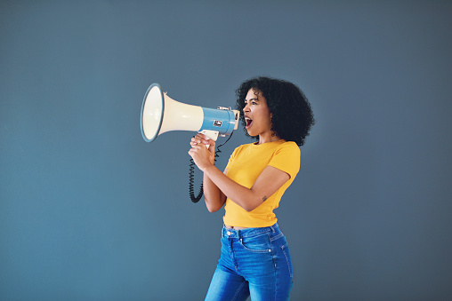 Cropped shot of an attractive young woman using a megaphone while standing against a grey background