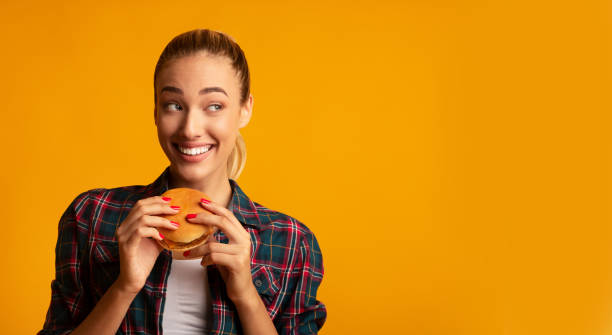 istock Young Woman Eating Burger In Studio, Yellow Background, Panorama 1173549014
