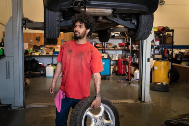 Ethnic young man mechanic with wheel in car workshop garage small business