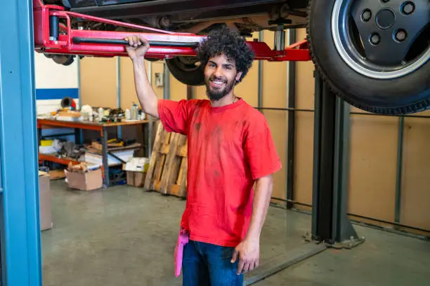 Ethnic young man mechanic smiling in car workshop garage small business