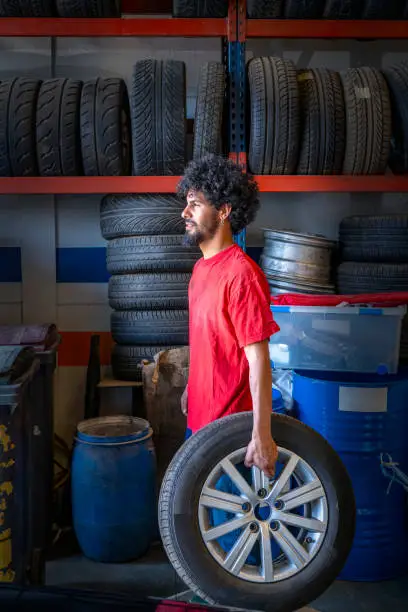 Ethnic young man mechanic with wheel in car workshop garage small business