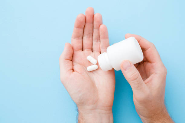 man spilling out white pills from bottle in his hand. receiving vitamins or medicaments. men's issues. medical, pharmacy and healthcare concept. point of view shot. pastel blue background. top view. - prescription doctor rx pharmacist imagens e fotografias de stock