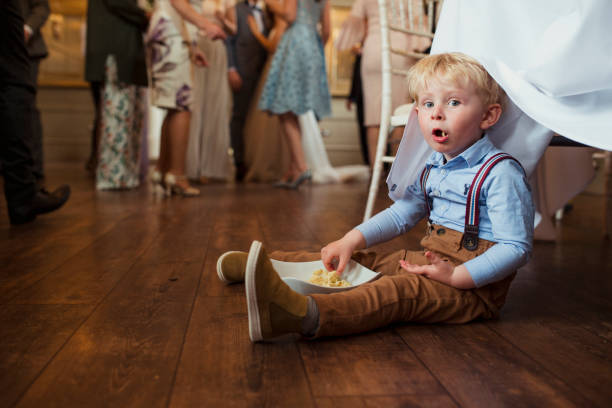 Sneaky Snacks Young boy sitting under a table at a wedding reception with a bowl of snacks. little boys blue eyes blond hair one person stock pictures, royalty-free photos & images