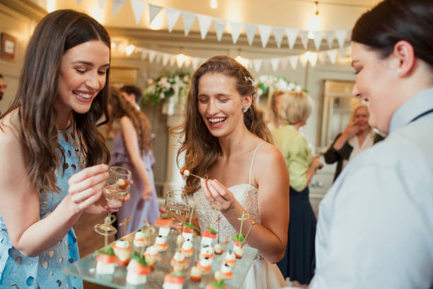 Trying The Canapés Bride and one of her guests at her wedding reception laughing and taking a canapé from a tray. canape stock pictures, royalty-free photos & images