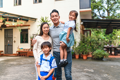 Mature Chinese mother and father standing with smiling young son and daughter outside their family home.