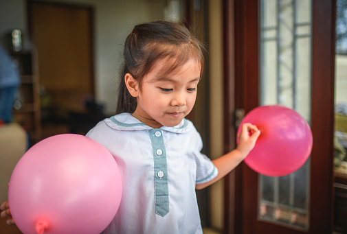 Close-up of contented young Chinese schoolgirl in uniform walking with two pink balloons after celebration.