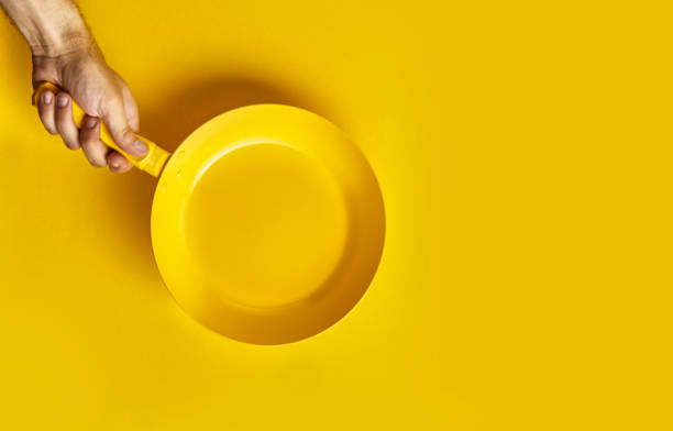 istock Colored pan in the hand. A hand is holding a yellow pan on a colored background. Colored pan isolated. Cooking food concepts 1173556494