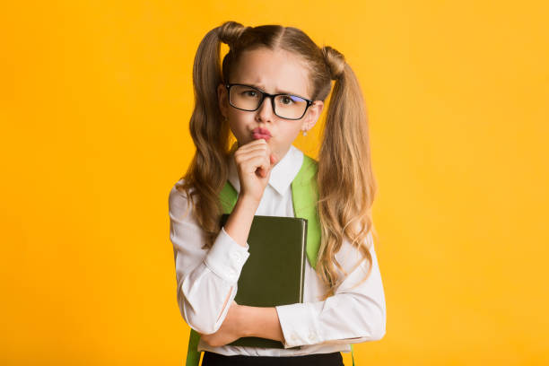 istock Cute Schoolgirl Thinking Touching Chin On Yellow Background 1173556543