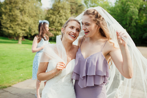 Bride and her sister outside with a veil wrapped around them laughing and smiling together.