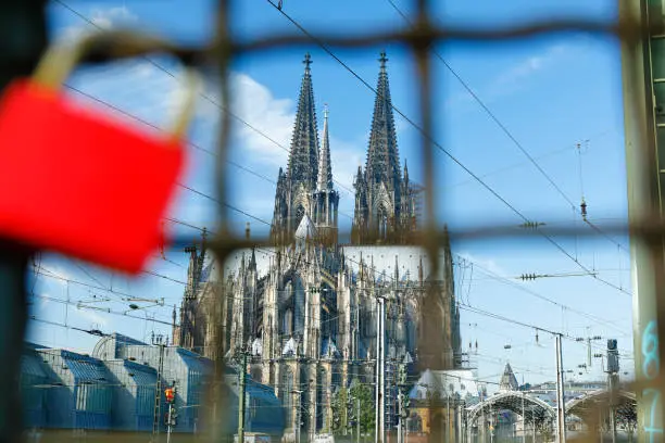 Cologne Central Station, the majestic Cologne Cathedral and a red love lock on iron fence in front.