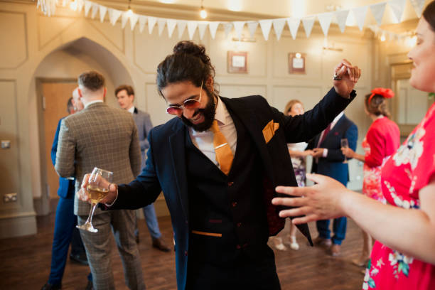 Letting Loose at a Wedding Reception Man at a wedding dressed in a suit and sunglasses dancing while other guests stand around him. He is holding a glass of wine and laughing. guest photos stock pictures, royalty-free photos & images