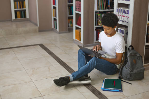 istock Young afro student using laptop, sitting on floor at library 1173560703