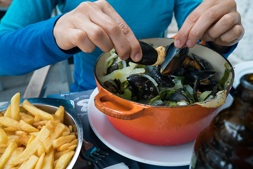 Horizontal view of hands of a woman eating traditional mussel and french fries dish called \