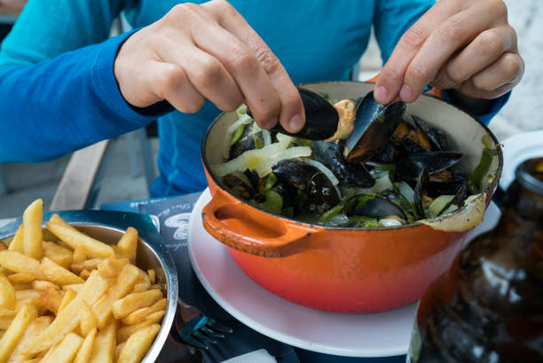 hands of a woman eating traditional mussel and french fries dish called "Moules et Frites" Horizontal view of hands of a woman eating traditional mussel and french fries dish called "Moules et Frites" moules frites stock pictures, royalty-free photos & images