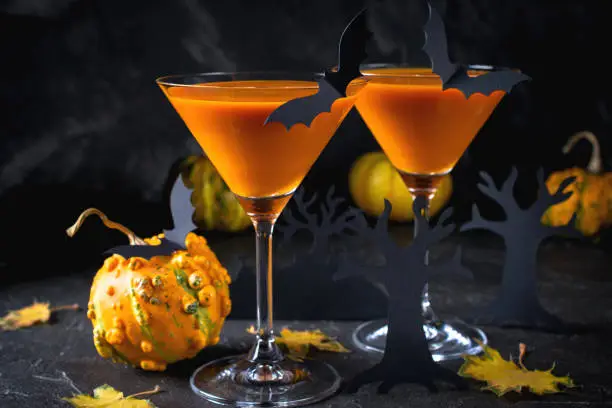 Photo of Orange martini cocktails with bats and decor for Halloween party, on dark background