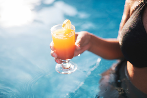 Unrecognizable woman hands with summer cocktail in pool, she holding elegance orange cocktail.