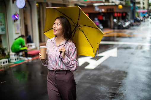 Beautiful cheerful Taiwanese woman walking on the street with umbrella on rainy day, smiling