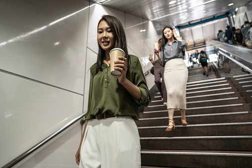 Young fashionable Asian girls moving down the stairs in subway, drinking coffee