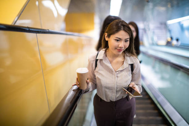 istock Asian woman on escalator using smart phone 1173564769