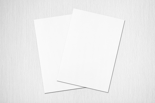 Two empty white rectangle poster or card mockups lying diagonally on top of each other with soft shadows on neutral light grey textured background. Flat lay, top view