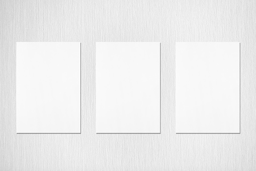 Three empty white vertical rectangle poster or card mockups with soft shadows on neutral light grey textured background. Flat lay, top view