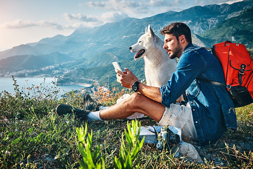 man relaxing and using his smartphone after hiking on the mountain with his dog