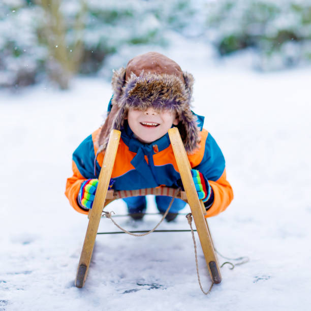 istock Little school boy having fun with sleigh ride during snowfall. Hapy child sledding on snow. Preschool kid riding a sledge. Child playing outdoors in snowy winter park. Active fun for family 1173571557