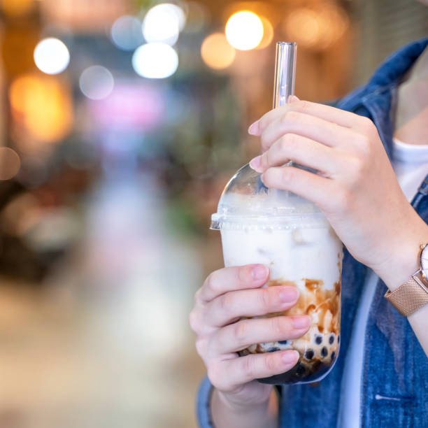 istock Young girl in denim jacket is drinking brown sugar flavored tapioca pearl bubble milk tea with glass straw in night market of Taiwan, close up, bokeh 1173571693