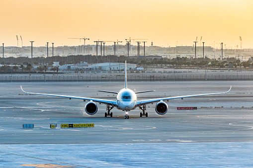 Front view of plane taxiing towards airport terminal at sunset - with construction cranes on horizon skyline