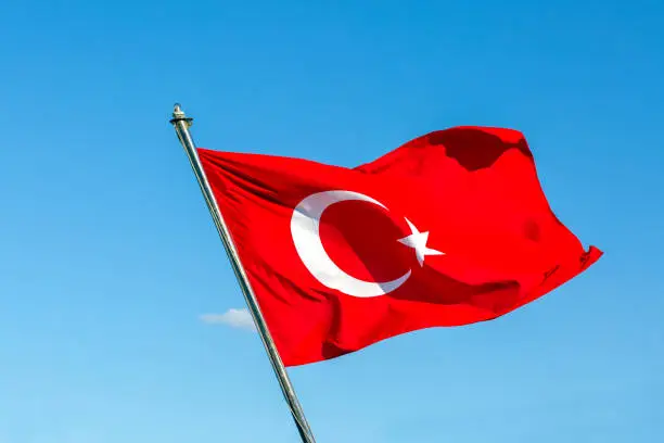 Waving Turkish Flag with clear blue sky on a sunny day in the background. Turkish flag consists of a crescent and a star inside it.