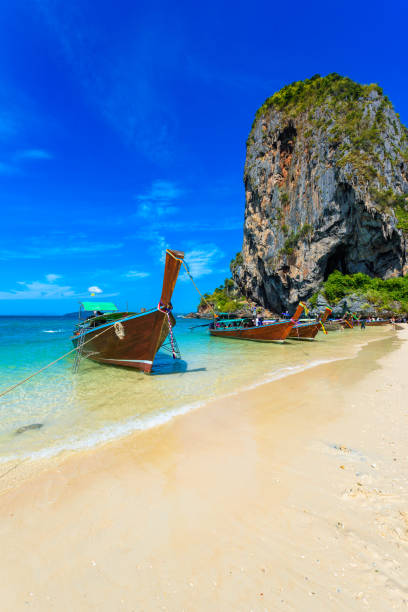 limestone karst rocks at ao phra nang beach with thai traditional wooden longtail boat on railay peninsula, close to ao nang, krabi province, andaman sea, thailand - phuket province beach blue cliff imagens e fotografias de stock