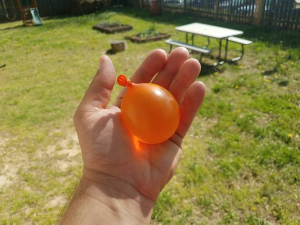 istock hand holding an orange water balloon over green grass 1173581270