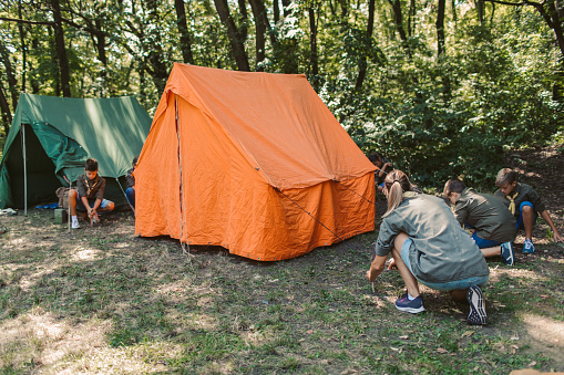 Group of scouts building a tent in forest.