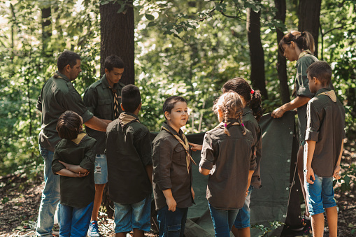 Group of scouts building a tent in forest.
