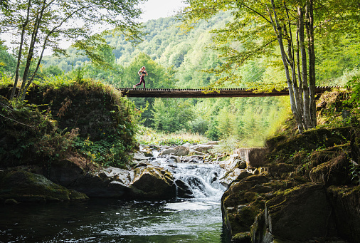 Woman running on wooden bridge in nature trails.